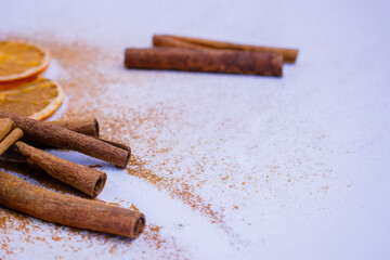 A pile of orange slices and cinnamon sticks on a white background. The oranges are cut in half and the cinnamon sticks are whole. Concept of warmth and comfort