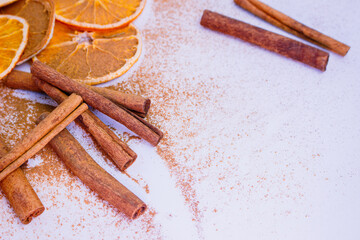 A pile of orange slices and cinnamon sticks on a white background. The oranges are cut in half and the cinnamon sticks are whole. Concept of warmth and comfort