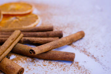 A pile of orange slices and cinnamon sticks on a white background. The oranges are cut in half and the cinnamon sticks are whole. Concept of warmth and comfort