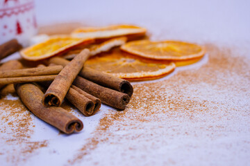 A pile of orange slices and cinnamon sticks on a white background. The oranges are cut in half and the cinnamon sticks are whole. Concept of warmth and comfort