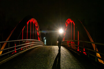 Stockholm, Sweden  A man walks over a an orange-lit pedestrian bridge in the Upplands Vasby district art night.