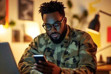 Fototapeta premium A bearded man wearing a camouflage jacket and glasses intently uses his smartphone, symbolizing focus and modern communication in a well-lit room.