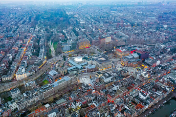 Obraz premium Vibrant aerial view of Amsterdam's Leidseplein district illuminated at dusk, showcasing iconic Dutch architecture, bustling nightlife, and serene green spaces