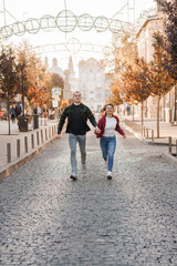 Joyful Young Couple Running Together on a Cobblestone Street in Autumn