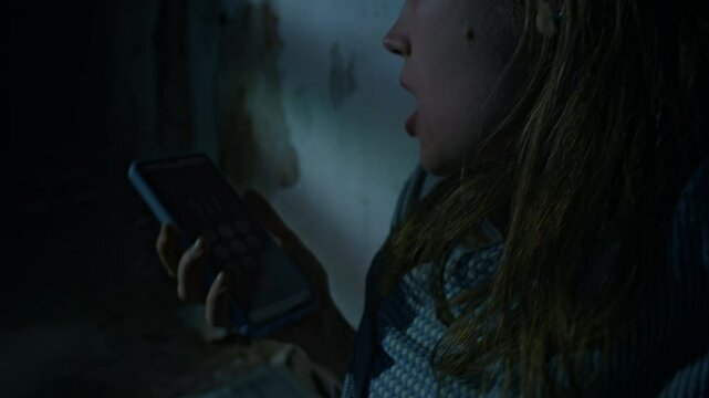 Side closeup of young Caucasian lady removing duct tape from mouth and quickly calling 911 using phone to get free from captivity, held hostage in abandoned basement, human abduction and trafficking