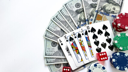 Poker chips, playing cards showing a royal flush in spades, red dice, and US dollar bills placed on a white background, representing gambling, luxury, and high-stakes poker. Ideal for casino advertise