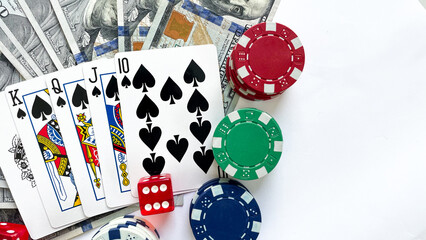 Fototapeta na wymiar Poker chips, playing cards showing a royal flush in spades, red dice, and US dollar bills placed on a white background, representing gambling, luxury, and high-stakes poker. Ideal for casino advertise