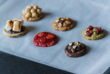 Homemade american round cookies with different toppings - raspberry, strawberry, pistachio, caramel, chocolate, peanuts, marshmallow, popcorn. Cookies on baking paper.