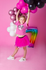 Happy Birthday. Happy girl laughs holding inflated balloons in her hands. Behind on a pink background is a multi-colored number seven..Emotions of happiness.