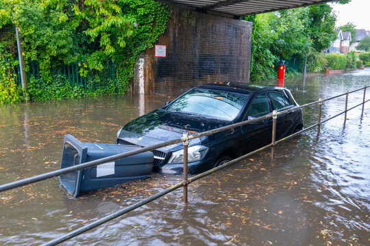 Flooded street with floating bin stuck in front of car, Sutton Coldfield, England, United Kingdom