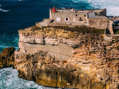 Aerial view of tourists at the historic Sao Miguel Arcanjo lighthouse overlooking Nazare's stunning coastline with giant waves, enjoying spectacular views, Nazare, Oeste, Estremadura, Portugal