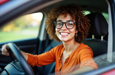 Young woman sits in car, smiles. Wears casual clothes, glasses. Holds steering wheel. Sunny day. Woman drives. Relaxed mood. Urban setting. Stylish look. Joyful expression. Modern transportation.