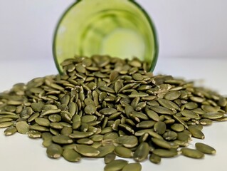 A close-up of a small pile of pumpkin seeds spread out on a pristine white surface, showcasing their natural texture and earthy green hues. These seeds are packed with nutrients, including zinc