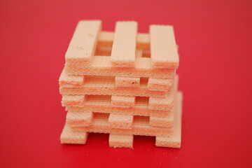 A pile of beige wafer cookies with a cream filling is scattered on a bright red surface
