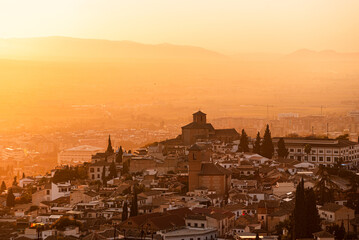 Hazy orange red sunset over Granada viewed from San Miguel Alto over the Albaicin alto and Iglesia de San Cristobal. Granada, Andalusia, Spain