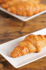 Artisan croissant handmade in a bakery. Close-up of croissant on a rectangular white plate. Continental breakfast, to be filled with sweet or savory ingredients.