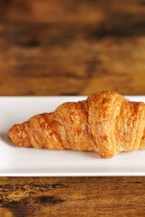 Artisan croissant handmade in a bakery. Close-up of croissant on a rectangular white plate. Continental breakfast, to be filled with sweet or savory ingredients.