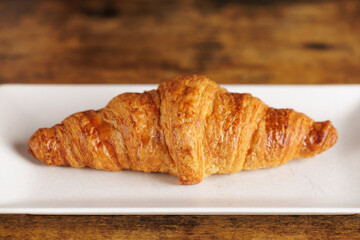 Artisan croissant handmade in a bakery. Close-up of croissant on a rectangular white plate. Continental breakfast, to be filled with sweet or savory ingredients.