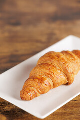 Artisan croissant handmade in a bakery. Close-up of croissant on a rectangular white plate. Continental breakfast, to be filled with sweet or savory ingredients.