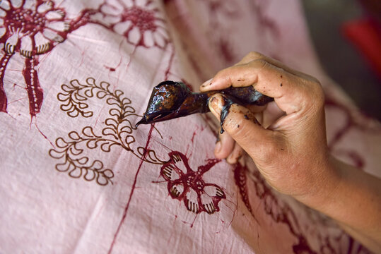 Woman using a pen-like tool (canting) to apply liquid hot wax to create pattern on the fabric before dyeing, workshop of Kidang Mas Batik House, Lasem, Java island, Indonesia, Southeast Asia