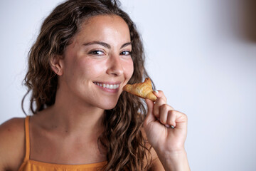 A smiling woman enjoys a snack in a cafe. The young woman tries a delicious croissant made by a pastry chef.