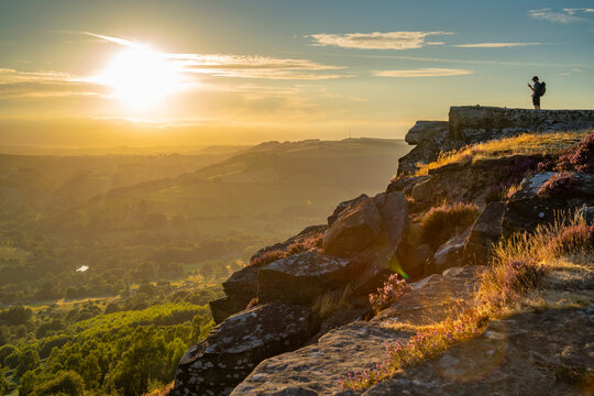 View of hiker viewing landscape from Curbar Edge at sunset, Peak District National Park, Baslow, Derbyshire, England, United Kingdom