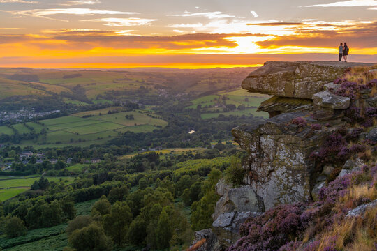 View of man and woman viewing landscape from Curbar Edge at sunset, Peak District National Park, Baslow, Derbyshire, England, United Kingdom