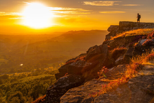 View of hiker viewing landscape from Curbar Edge at sunset, Peak District National Park, Baslow, Derbyshire, England, United Kingdom