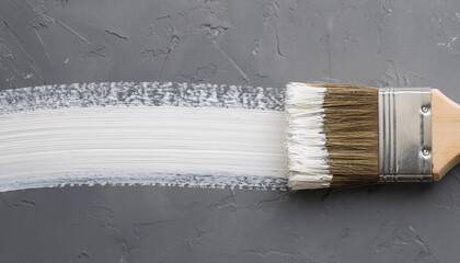 Brush with white paint and brushstroke on gray background. Top view.