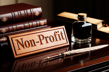 A wooden word text Non-Profit inscribed on it, placed on a wooden table along with a feather quill, an ink bottle, and a stack of leather-bound books.