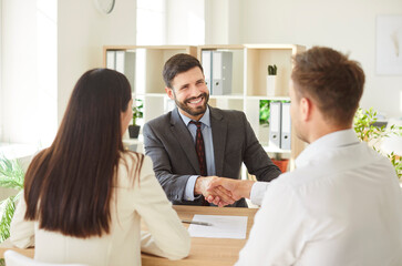 Husband and wife, as clients, shake hands with an agent or consultant during meeting in an office...