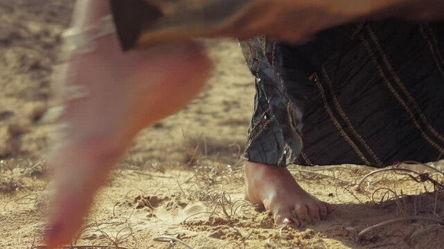 Close-up of woman feet, decorated with anklets, walking barefoot across sandy, rocky desert landscape, highlighting nature beauty and freedom of movement in tranquil setting