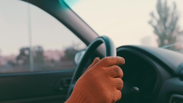 Close-up shot of construction worker impatiently tapping steering wheel with work glove, rushing between job sites at sunset