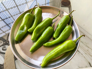 Fresh green Kashmiri mirch arranged neatly on a steel plate, their glossy, vibrant skin showcasing a mild yet flavorful spice.