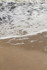 Detailed view of foamy ocean water gently meeting the smooth sand on a sunny beach day.