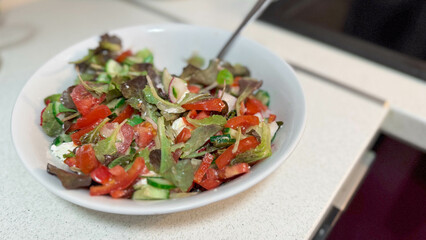 Close-up photo of white ceramic plate with natural fresh vegetable salad. Cucumbers, tomatoes, greens and white Greek feta cheese.