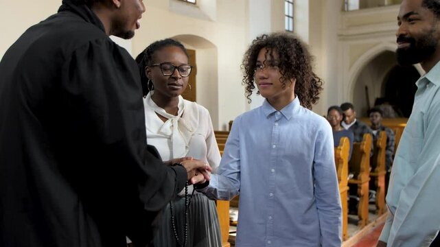 Priest congratulating teenage boy after confirmation in church