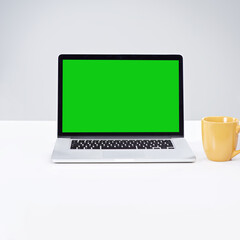 Laptop, green screen and coffee on desk for space, mockup and online on white studio background. Blank tech, computer monitor and table for advertising cup, digital marketing and commercial promotion