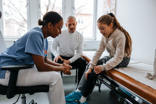 Girl with artificial limb talking to female pediatrician while sitting on bed in examination room