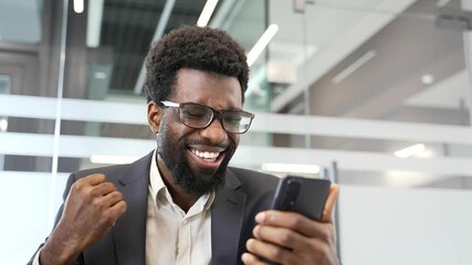 Happy excited african american businessman in formal suit receiving good news on phone sitting in business office. Satisfied handsome bearded entrepreneur expressing happiness and success. Close up