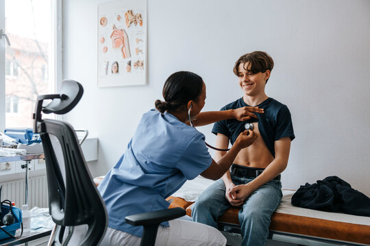 Female medical expert checking boy's chest with stethoscope while sitting on chair in examination room