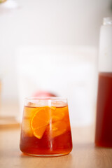 Glass of fresh cold brew coffee or cocktail with ice and slice of orange placed on wooden kitchen worktop with white background.
