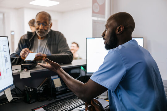 Senior man doing payment through smart phone at reception desk in medical clinic