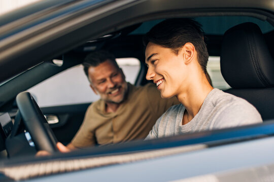 Happy young man learning to drive while sitting with father in car