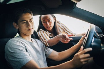 Mother instructing driving lessons to son sitting in car