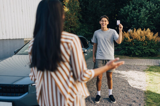 Happy young man showing drivers license to mother standing in back yard