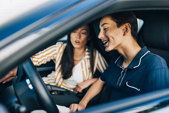 Happy teenage boy getting driving lessons from mother while sitting in car