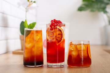 Combo of three glasses of fresh cold brew coffee, lemonade and an cocktail with ice and slice of orange and fresh mint leaves decoration, placed on wooden kitchen worktop with white background.