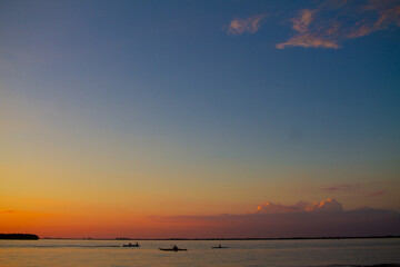 Fototapeta premium A serene sunset over the river with the horizon line low in the frame. The vast, nearly cloudless sky dominates the scene, blending warm and cool tones in an abstract, painterly style