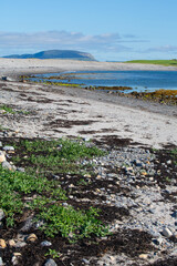 dark pebbles on light sand against a blue sky and sea